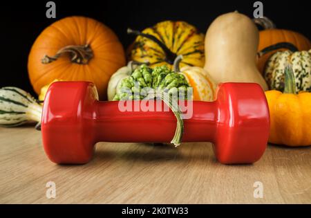 Manubri con varietà di zucche o zucche commestibili e decorative. Stile di vita sano autunno composizione autunno. Allenamento in palestra, concetto di allenamento fitness. Foto Stock