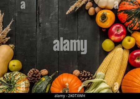 Struttura autunnale piatta con zucche, noci, coni, mele, frutta kaki persimmon, mais sulla pannocchia. Copia spazio su sfondo di legno. Foto Stock