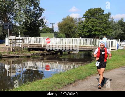 Un corridore sorridente passa il ponte di oscillazione di Crabtree Lane partecipando alla corsa di lunga distanza del canale Liverpool a Leeds 2022 in un giorno soleggiato di agosto. Foto Stock