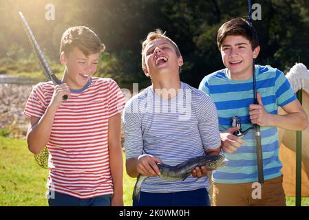 Theres qualcosa di pesce che sta succedendo qui... tre ragazzi che ridono mentre si levano in piedi con il pesce che hanno catturato. Foto Stock