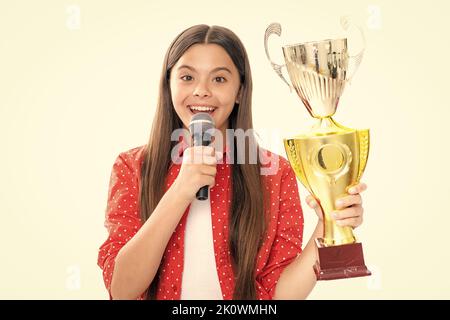 Ragazza con microfono a coppa di vincita discorso. Teen che tiene un trofeo. Bambino vincitore del capretto ha vinto la concorrenza, celebrando il successo e la vittoria. Ritratto di felice Foto Stock