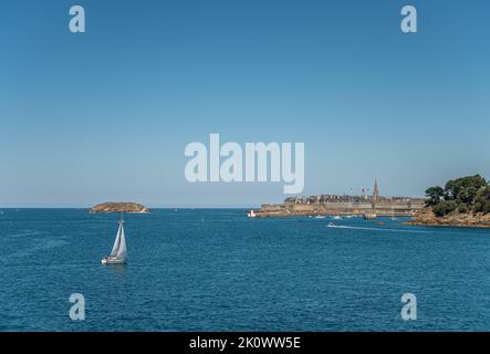 St. Malo, Bretagna, Francia - 8 luglio 2022: Centro storico con i suoi alti palazzi dietro i suoi bastioni, che sporgono nel canale della Manica sotto il cielo blu Foto Stock