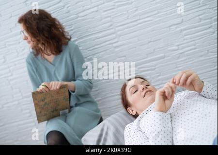 Una donna di mezza età si trova su un divano e parla con uno psicologo. Foto Stock