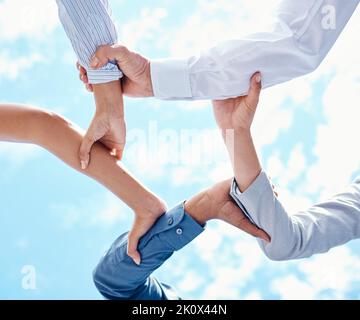 Lavoro di squadra, mani e collaborazione con un team di uomini d'affari che tengono le braccia in un cerchio o si accoccolano su un cielo blu dal basso. Motivazione, fiducia e. Foto Stock