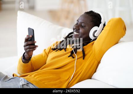Ritratto dell'uomo Nero sorridente indossando cuffie rilassanti con lo smartphone a casa Foto Stock