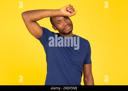 Uomo afroamericano sportivo che puliscono il sudore dalla fronte, sfondo giallo Foto Stock