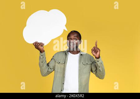 Ho idea. Sorridente uomo nero maturo in casual tenere bolla nuvola astratta con spazio vuoto e mostrando dito in su Foto Stock