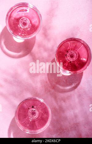 Champagne rosa in bicchieri su tavolo in marmo rosa con ombra di palma. Cocktail party estivo in spiaggia con vino di rosa, bevande alcoliche su sfondo testurizzato w Foto Stock