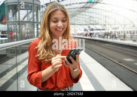 Sorridente viaggiatore brasiliano attraente passeggero acquista il biglietto online con smartphone in stazione ferroviaria. Spazio di copia. Foto Stock