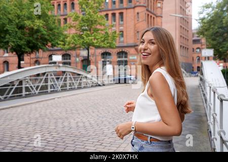 Attraente donna positiva si gira intorno e guardando al lato in una strada di città del Nord Europa Foto Stock