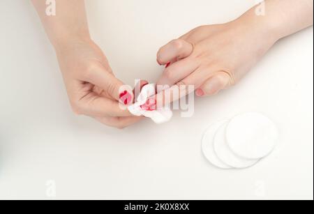 Una vista dall'alto di una donna che rimuove smalto sulle dita utilizzando tamponi di cotone su uno sfondo bianco Foto Stock