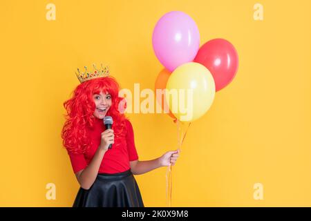 bambino felice in corona con microfono e festa balloon su sfondo giallo Foto Stock