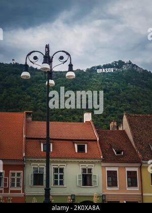 La città vecchia di Brasov con colorati edifici vintage in stile tradizionale sassone con vista sul cartello in cima alla collina. Popolare località turistica Foto Stock