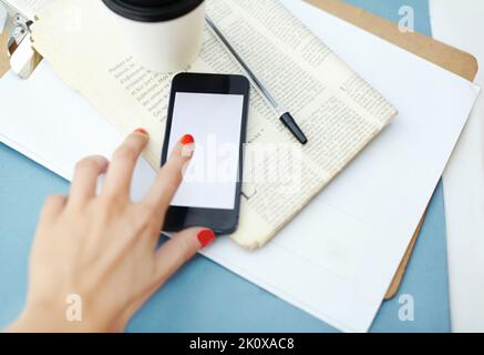 Controllare qualcosa appena letto. Tazza monouso in cima a un giornale e alla clipboard, con una penna e uno smartphone. Foto Stock