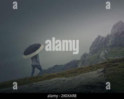 La vista posteriore di un uomo solitario con ombrello si erge su una collina rocciosa coperta da foschia. Moody e scena emotiva con una silhouette strana solita sotto la pioggia Foto Stock