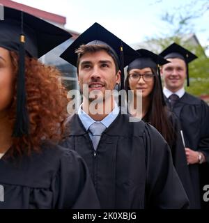 Continua a impegnarsi per ottenere risultati migliori. Studenti universitari in una graduazione giorno in piedi in una fila. Foto Stock