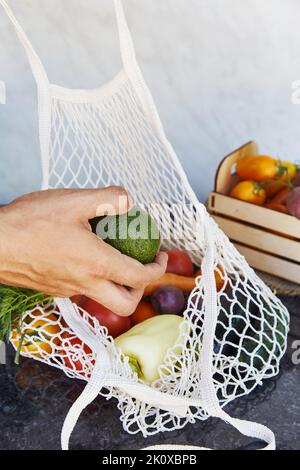 L'uomo mette l'avocado al sacchetto eco-stringa con verdure fresche - pomodori, patate viola, melanzane, carote, pepe dolce. Preoccupazione ecologica, eco sh Foto Stock