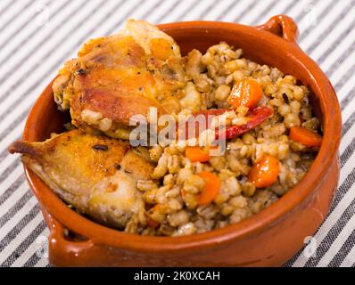 Porridge d'orzo con cosce di pollo in recipiente di ceramica Foto Stock