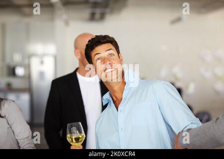 Freakout booze gratuito. Un uomo ubriaco che tiene un bicchiere di vino e tira i volti in un ufficio sociale. Foto Stock