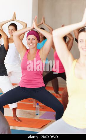 Posizione perfetta per lo yoga. Un gruppo di sorridenti studenti di yoga accovacciati con le mani sollevate sopra la testa. Foto Stock