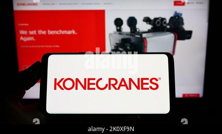 Persona che tiene uno smartphone con il logo della società di gru finlandese Konecranes Oyj sullo schermo di fronte al sito Web. Messa a fuoco sul display del telefono. Foto Stock