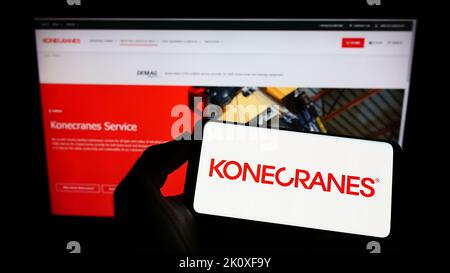 Persona che tiene il telefono cellulare con il logo della società finlandese di gru Konecranes Oyj sullo schermo di fronte alla pagina web aziendale. Messa a fuoco sul display del telefono. Foto Stock