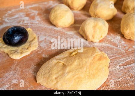 Pezzo di lievito, susina, gnocchi di prugne su tavola di legno da cucina cosparso di farina, primo piano. Preparazione di gnocchi di prugne dolci. Foto Stock