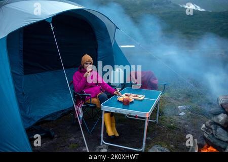 Donna, seduta intorno al fuoco di notte, godendo campeggio selvaggio, vacanza in famiglia in Norvegia estate Foto Stock