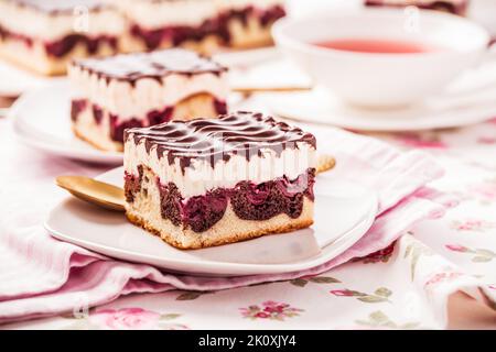 Torta tedesca Donauwelle (onde del Danubio) - torta di Spagna alla vaniglia e al cioccolato con ciliegie acide, crema di burro alla vaniglia e glassa al cioccolato con tazza di tè Foto Stock