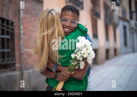 Amici multietnici felici abbracciando mentre tiene un bouquet di fiori in strada Foto Stock