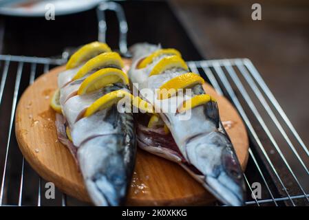 Sgombri con fettine di limone su un tagliere di legno, vista dall'alto. Il processo di cottura del pesce all'aperto. Cibo gustoso e fresco, picnic, festa, outdoo Foto Stock