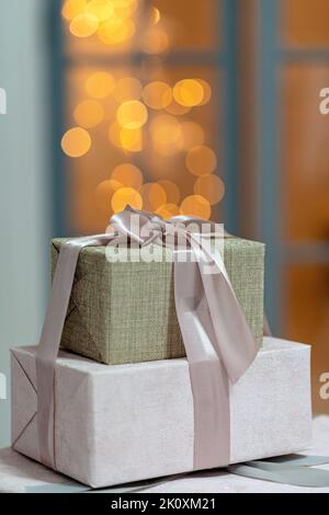 Primo piano di confezioni regalo confezionate in modo festivo, su uno sfondo natalizio di luci scintillanti, un magico sfondo del Capodanno. Sfocatura, messa a fuoco selettiva morbida Foto Stock