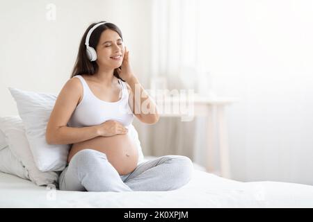 Felice bella giovane donna incinta che ascolta la musica in cuffie Foto Stock