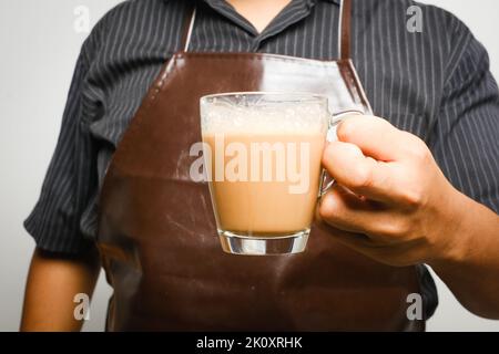 Immagine selettiva di messa a fuoco della mano che tiene 'tarik' con gli uomini preparato la bevanda Insight. Il tè dolce al latte è stato tirato per mescolare bene e creare schiuma Foto Stock