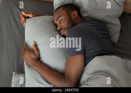 Stanco Africano maschio mentire avendo insonnia in camera da letto, angolo alto Foto Stock