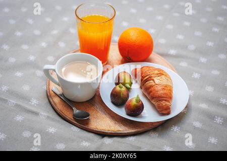 Mattina, deliziosa colazione a letto. Croissant su un piatto con fichi, una tazza da caffè, succo d'arancia e un'arancia su un vassoio primo piano. Foto Stock