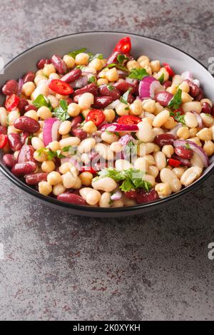 Insalata di tre fagiolini con ceci, cipolle, peperoncini e olio d'oliva in un recipiente sul tavolo. Verticale Foto Stock