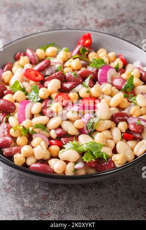 Tre insalata di fagioli con peperoncino e cipolla delizioso cibo vegetariano primo piano in un piatto sul tavolo. Verticale Foto Stock