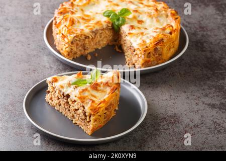 Deliziosa torta di spaghetti con carne macinata, salsa di pomodoro e parmigiano e mozzarella primo piano in un piatto sul tavolo. Orizzontale Foto Stock