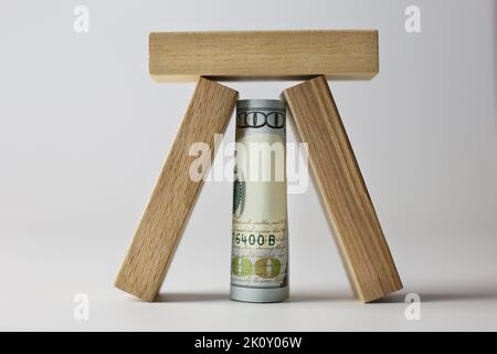 Arrotolato su 100 dollari di legge coperto con cubi di legno su uno sfondo chiaro. Concetto di valuta Foto Stock