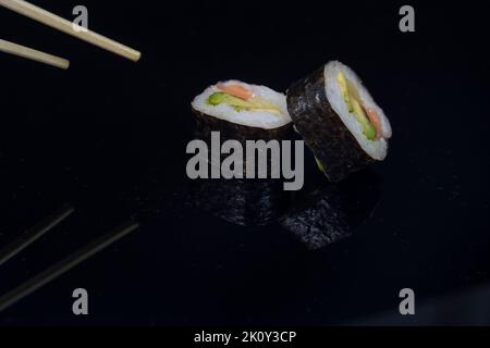 due pezzi di sushi con bacchette su sfondo scuro Foto Stock