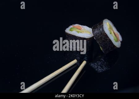 due pezzi di sushi con bacchette su sfondo scuro Foto Stock