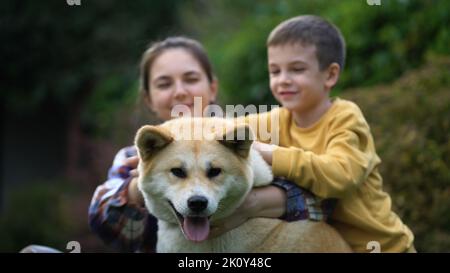 Famiglia in cortile giocando con il cane Akita Inu. Mamma e figlio accarezzano e abbracciano il loro cane. Foto Stock