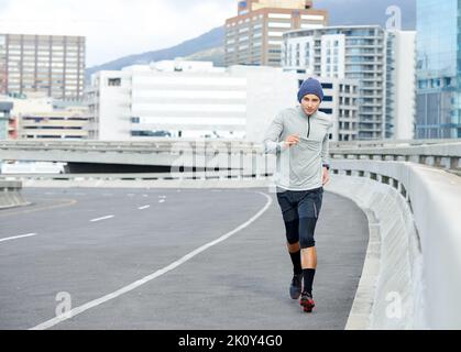 Correre attraverso la giungla urbana, un giovane che fa jogging per le strade vuote della città. Foto Stock