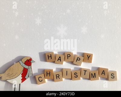 Buon Natale in 3D lettere di alfabeto di legno con un robin di legno, isolato su uno sfondo bianco con fiocchi di neve e spazio copia Foto Stock