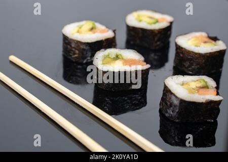 cinque pezzi di sushi con bacchette su sfondo scuro Foto Stock