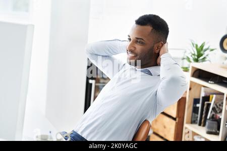 Prenderlo facile. Un bel giovane uomo d'affari afroamericano seduto alla sua scrivania e rilassante. Foto Stock