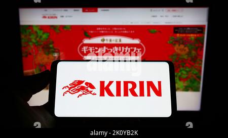 Persona che tiene il cellulare con il logo della Kirin Brewery Company giapponese Limited sullo schermo di fronte alla pagina web aziendale. Messa a fuoco sul display del telefono. Foto Stock