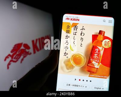 Persona che tiene il cellulare con il sito web della Kirin Brewery Company giapponese Limited sullo schermo di fronte al logo. Messa a fuoco al centro del display del telefono. Foto Stock