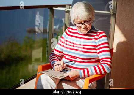 Donna anziana in bicchieri seduti sul balcone vicino al mare Foto Stock